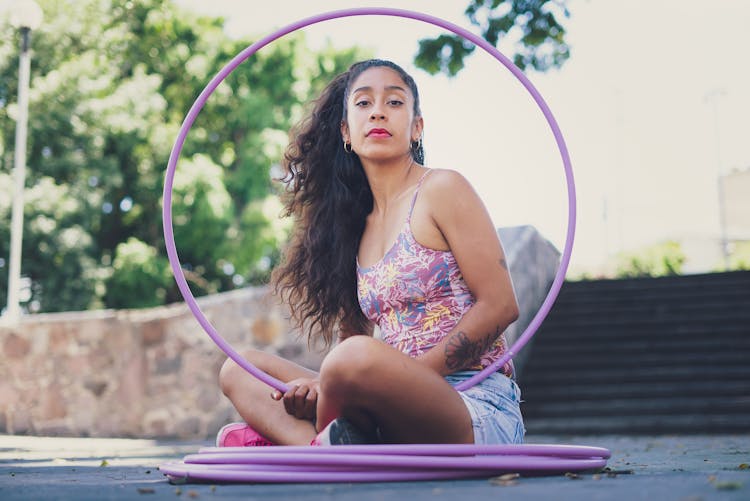 A Woman In Floral Tank Top Sitting While Holding A Hula Hoop