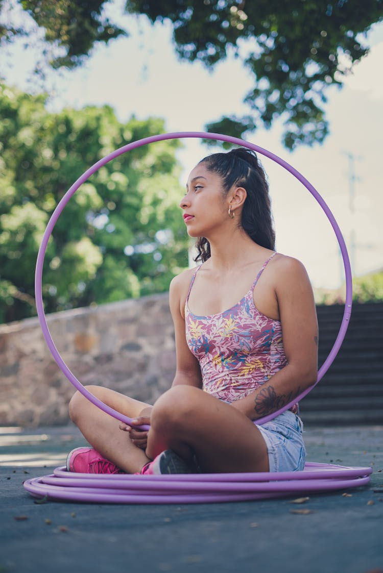 A Woman In Floral Tank Top Sitting On The Floor While Holding A Hula Hoop