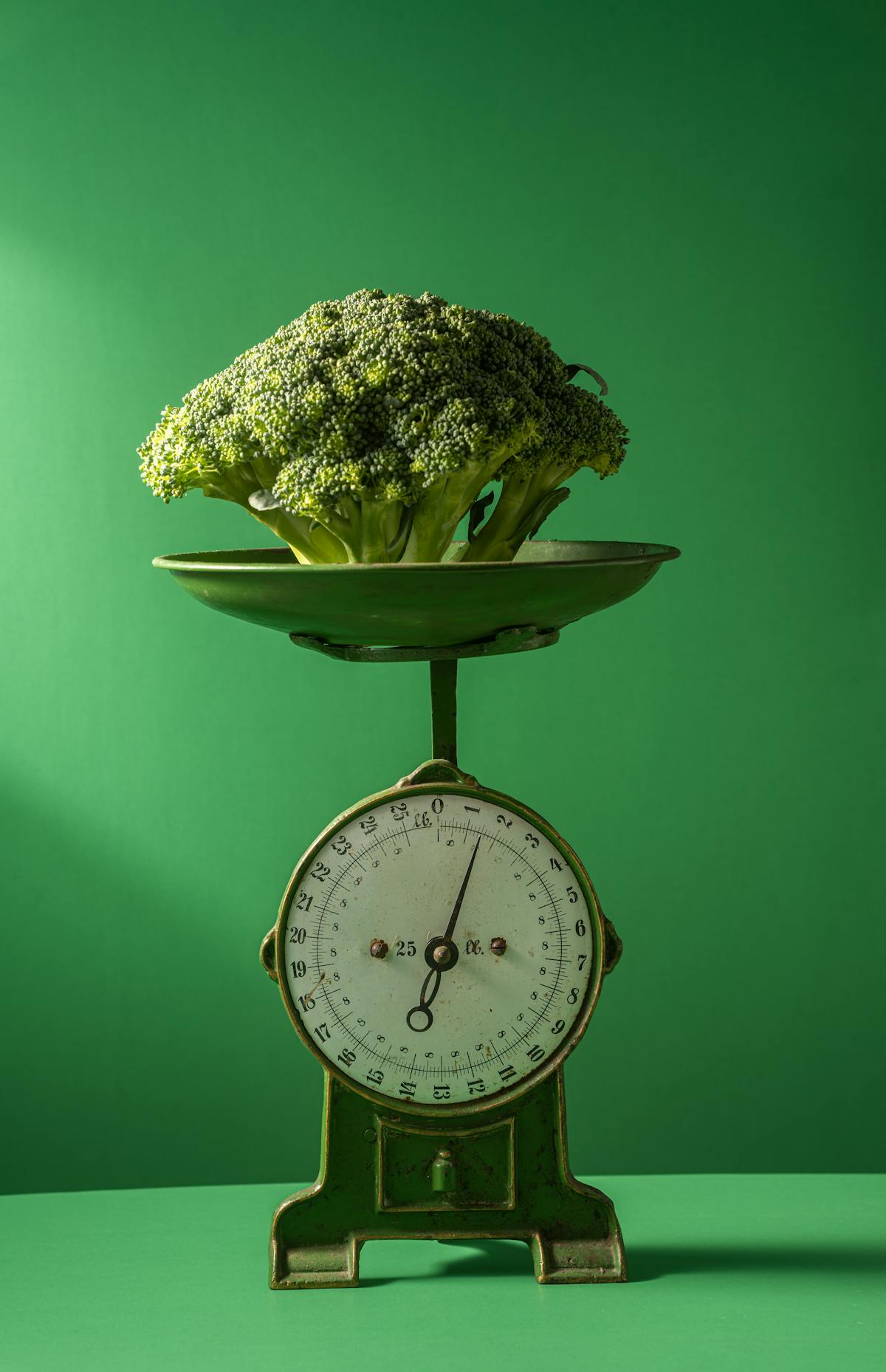 Fresh broccoli displayed on a vintage green weighing scale against a green background
