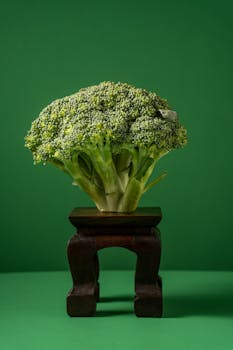 Artistic still life of fresh broccoli on a wooden stand with a green background.
