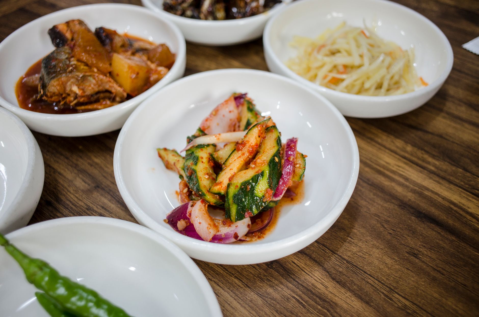 A selection of colorful Korean side dishes, including kimchi and vegetables, on a wooden table.