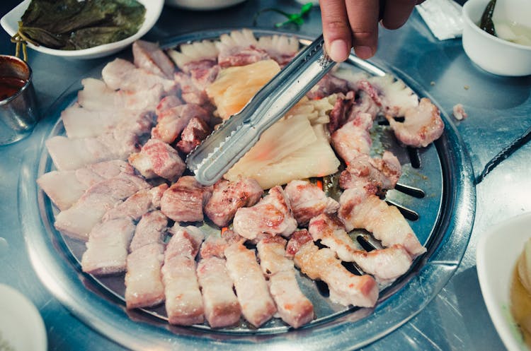 Person Holding Tongs Cooking Meat On A Griller