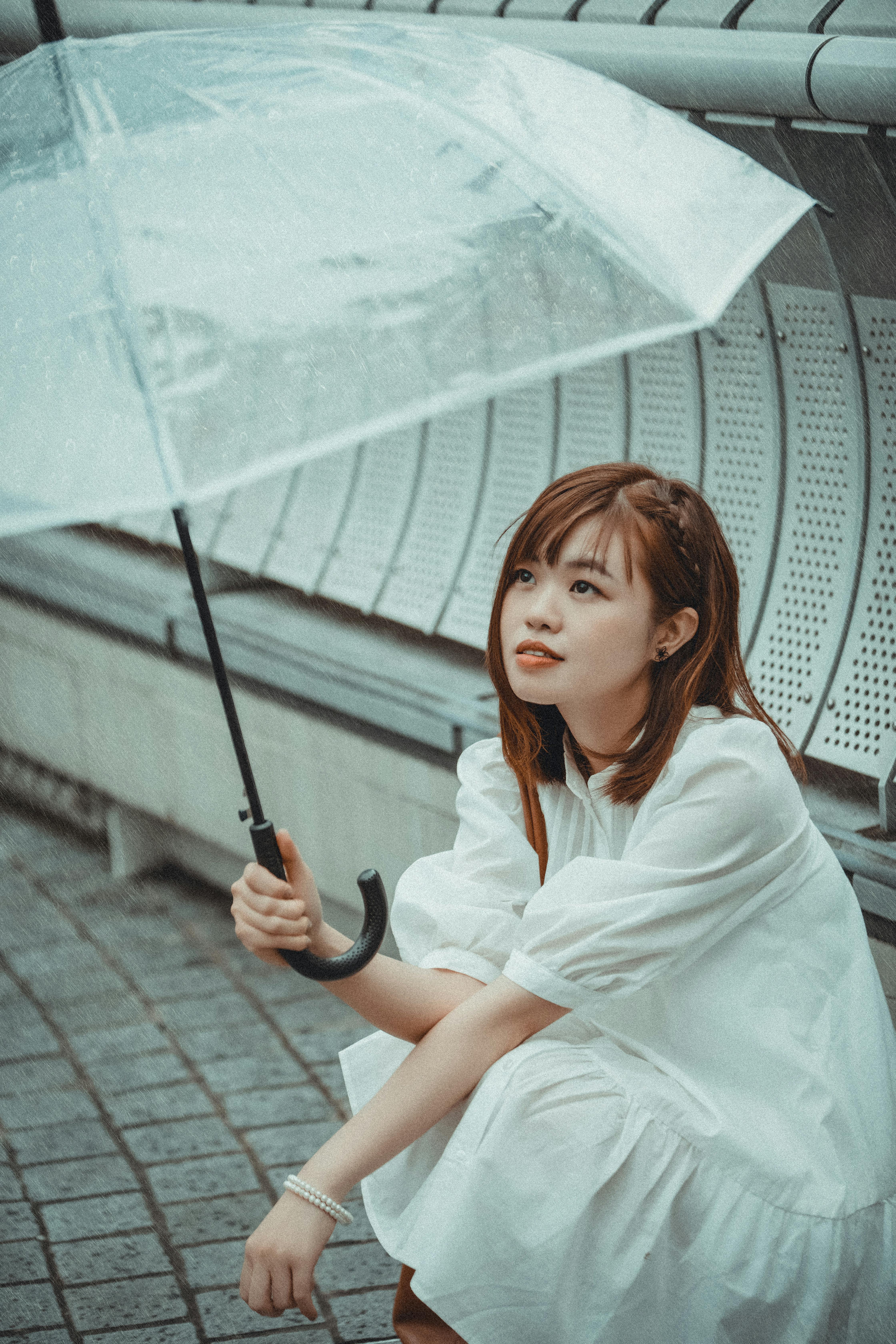 Asian woman in white dress holding umbrella by metal railings outdoors.