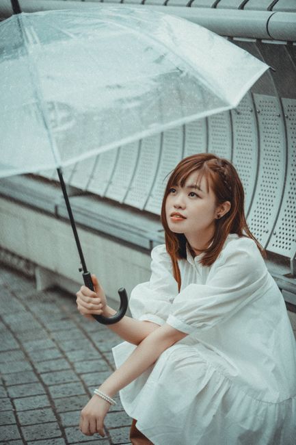 Asian woman in white dress holding umbrella by metal railings outdoors.