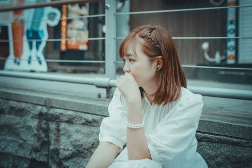 Free Woman in white dress and pearl bracelet sitting pensively outdoors. Stock Photo