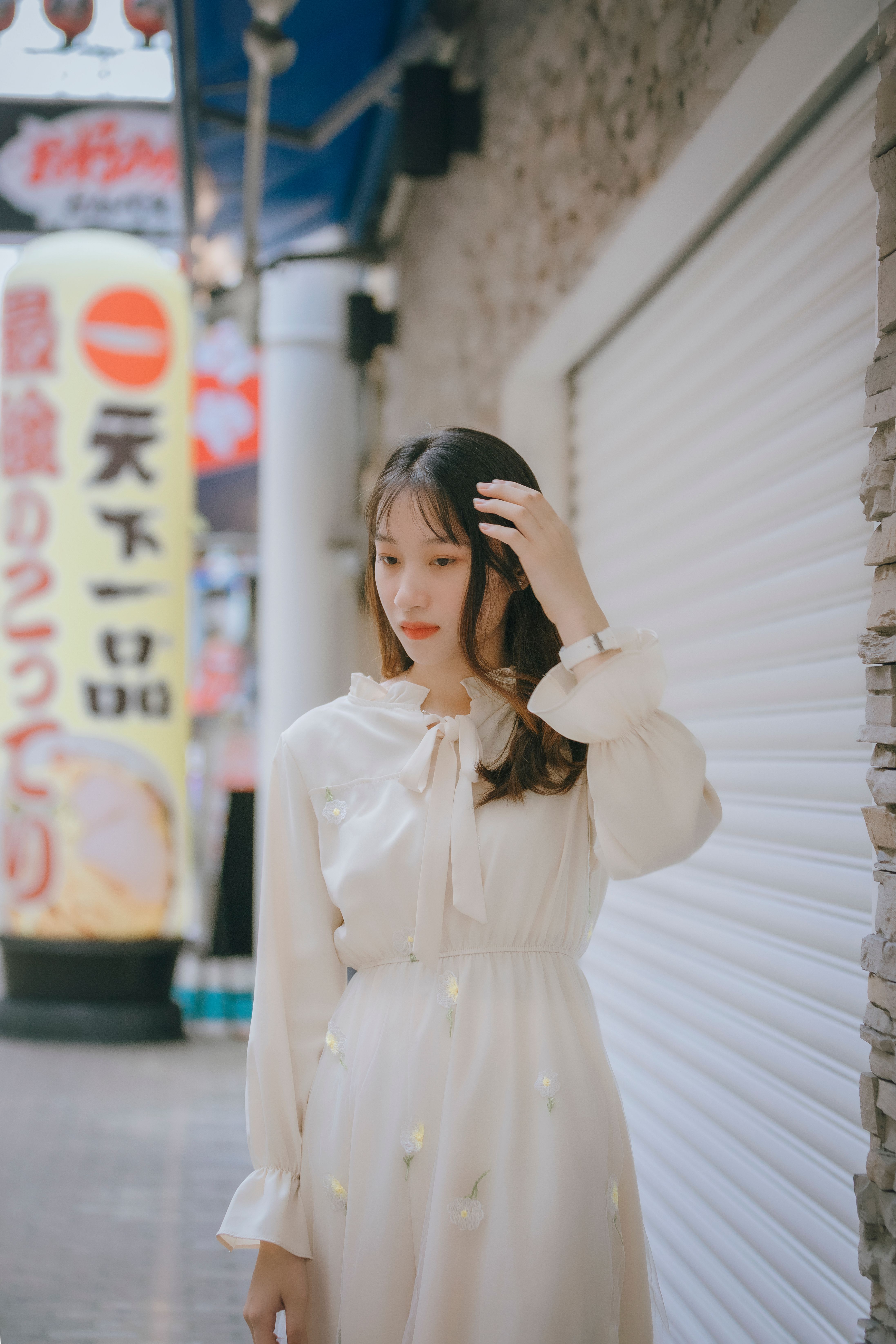 Portrait of a woman in a white dress walking down a vibrant city street with a colorful sign in the background.