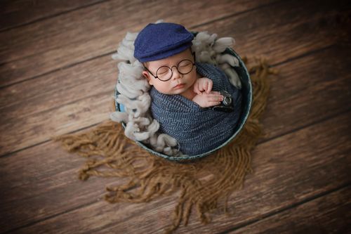 Free Adorable baby peacefully sleeping in a cozy hat and glasses, wrapped in a swaddle on rustic wooden floor. Stock Photo