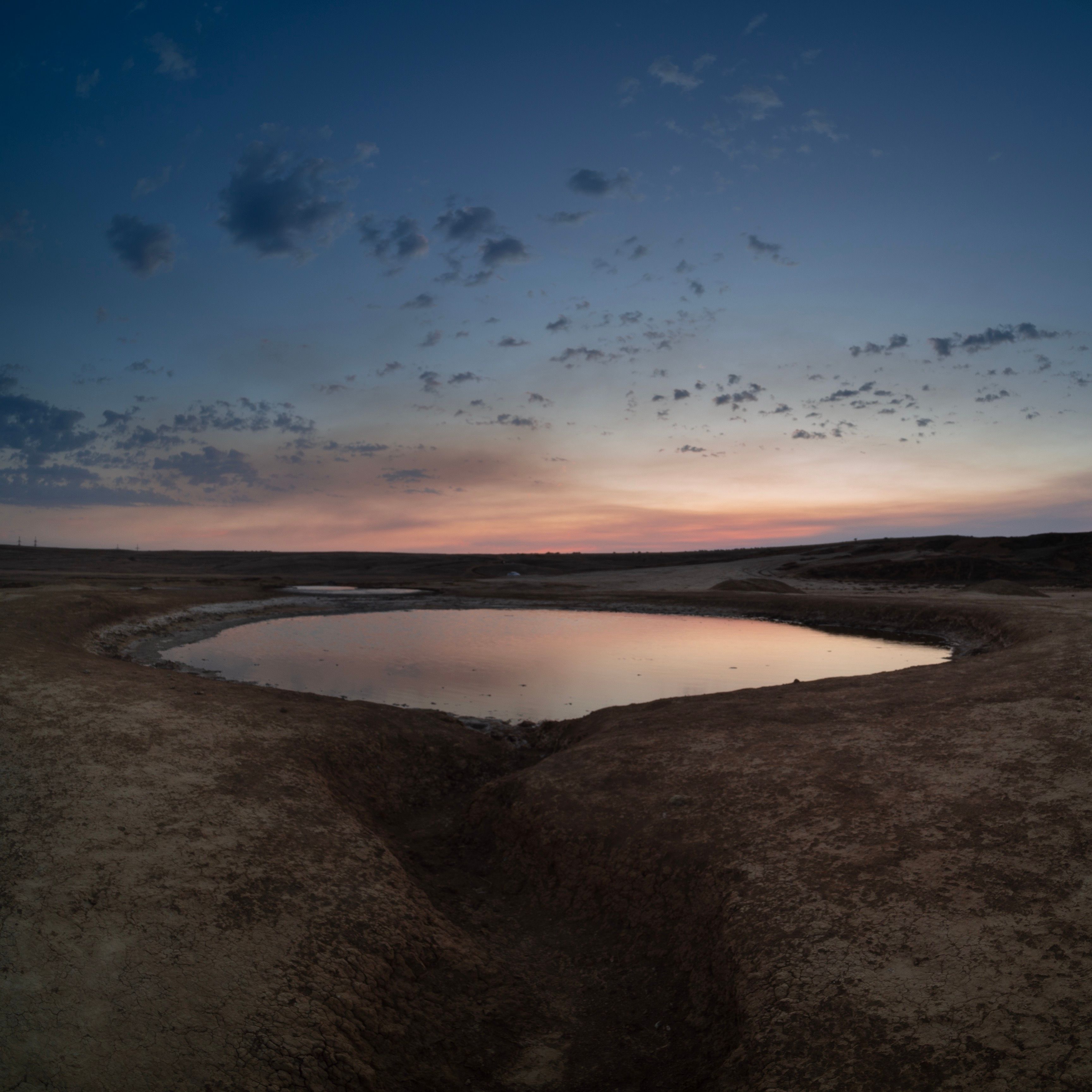 A serene lake surrounded by dirt ground reflecting the colorful twilight sky.