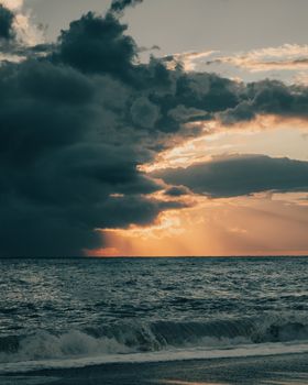 Captivating sunset over the ocean with dramatic clouds and crashing waves.