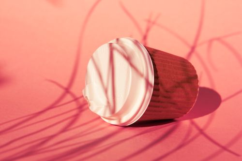 Free Stylish disposable coffee cup with lid, casting shadows on a pink background. Stock Photo