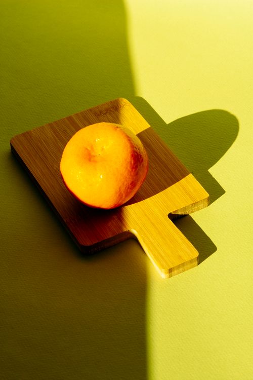 Free Bright orange fruit resting on a wooden cutting board, casting a shadow, vibrant and minimalistic. Stock Photo