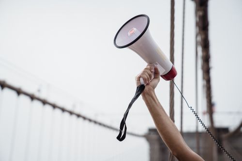 Free A hand holding a megaphone, symbolizing protest or announcement at an outdoor rally. Stock Photo