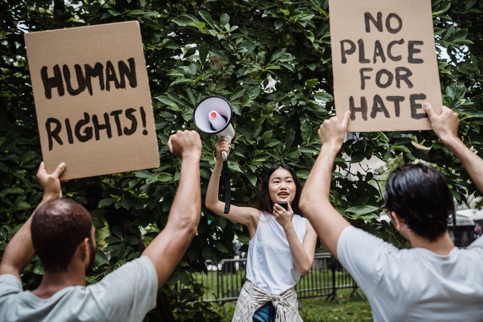 A diverse group of people protesting with signs advocating for human rights and against hate.
