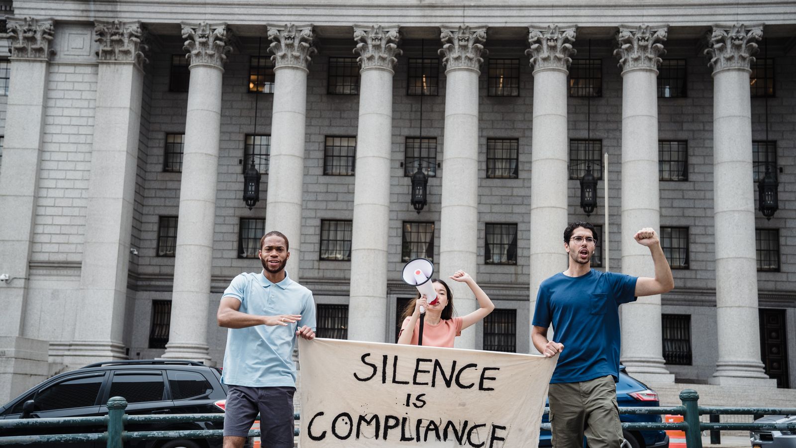 Three protesters with a 'Silence is Compliance' banner in front of a courthouse.