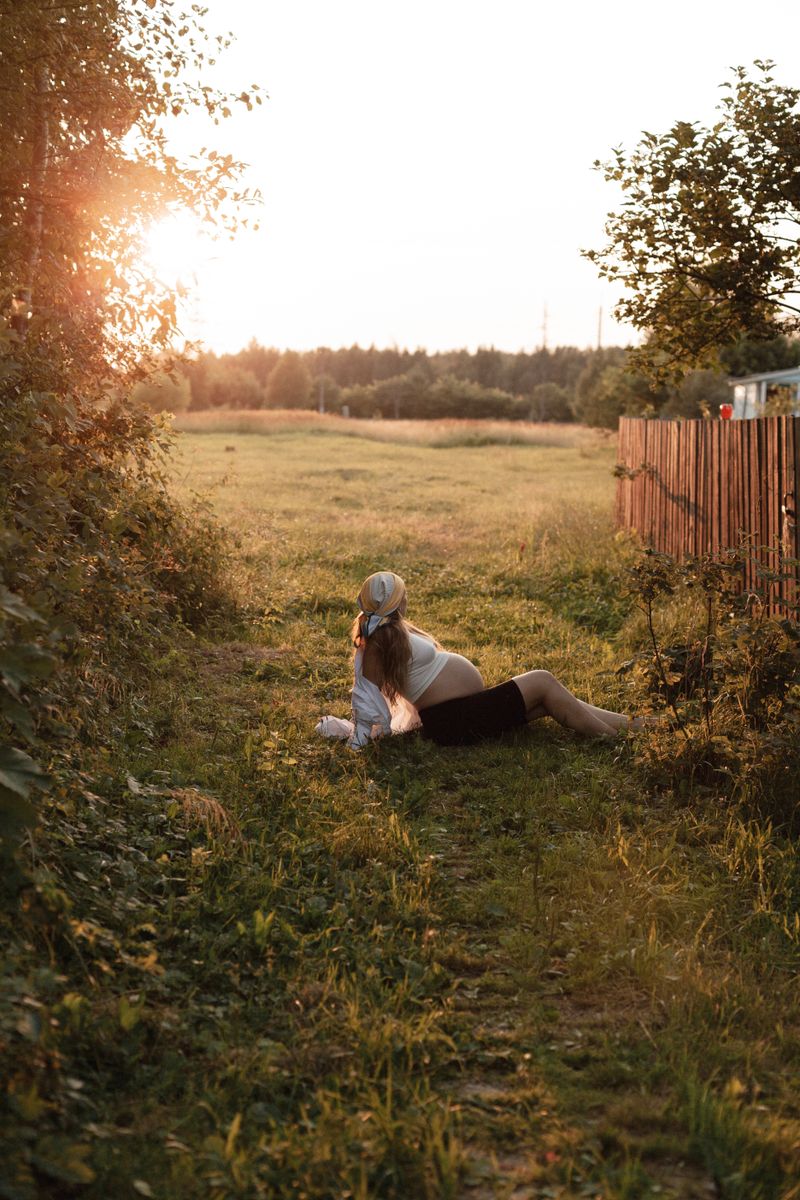 Pregnant woman lounging in a grassy field during sunset, enjoying peaceful nature.