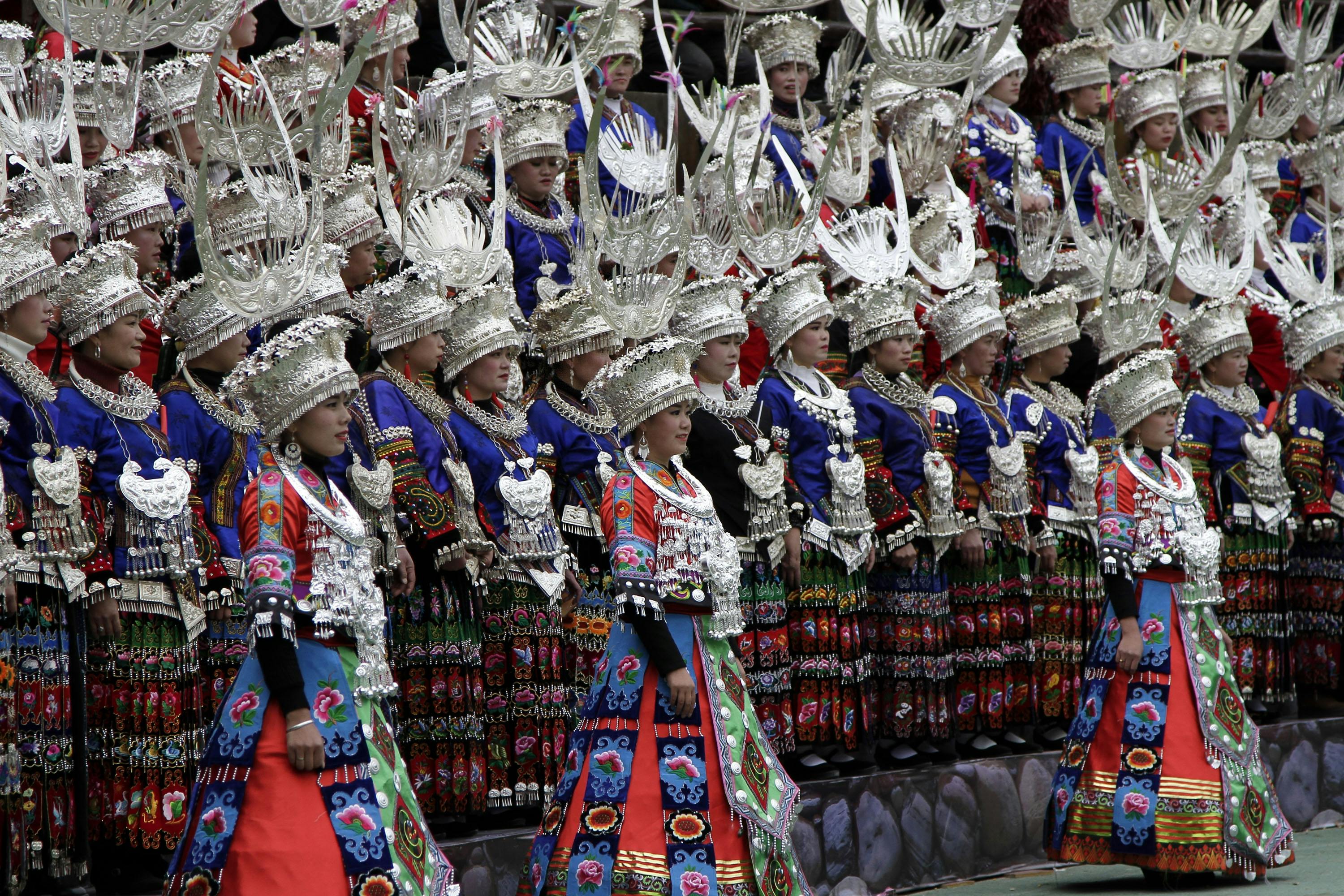 Group of women in traditional Chinese attire during a cultural ceremony, showcasing intricate silver headdresses and colorful garments.