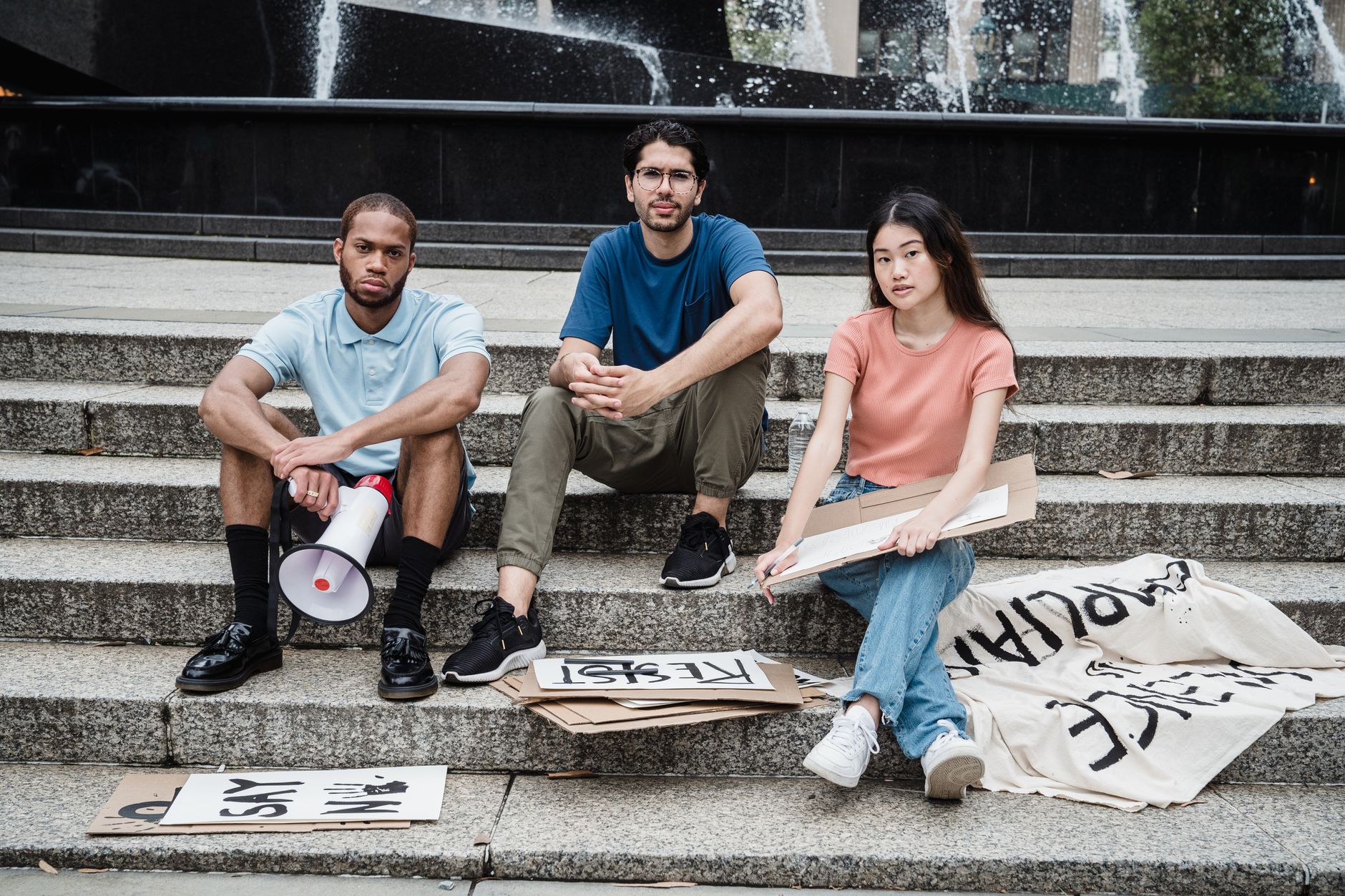 Three young activists with protest signs seated on concrete steps, symbolizing unity and peaceful protest.