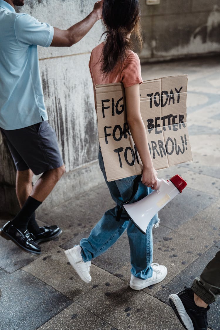 Young Woman And Man Walking In A Protest Holding A Loudspeaker And A Cardboard Banner 