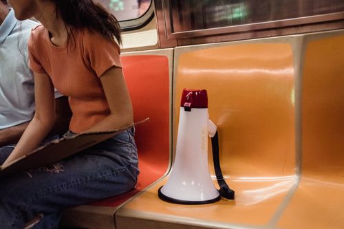 Free A megaphone resting on a colorful subway seat, with a person nearby holding a clipboard. Stock Photo