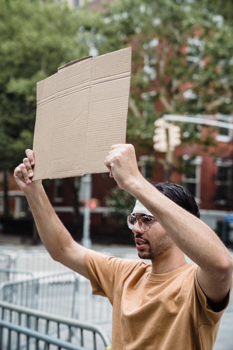 Man In A Brown Shirt Holding A Cardboard Sign