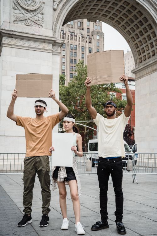 Free Three diverse individuals holding blank placards under a city arch, promoting peaceful protest. Stock Photo