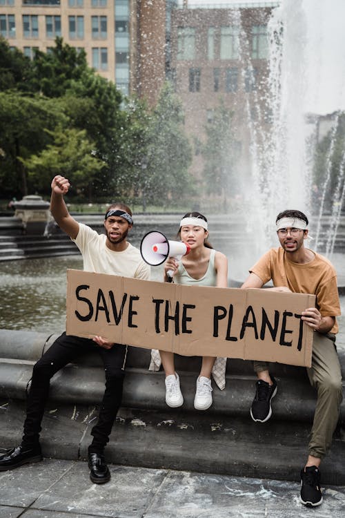 People holding a Slogan sitting on a Water Fountain 