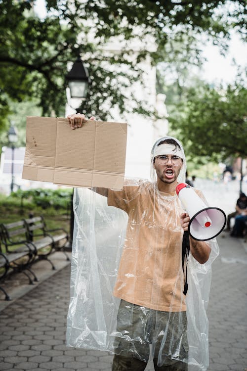 Man Using a Megaphone while Holding a Cardboard Sign