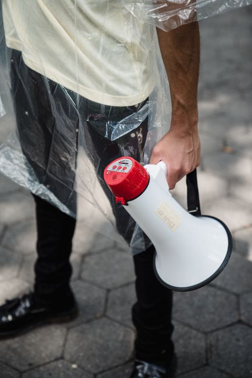Free A partial view of a person holding a megaphone wrapped in a plastic sheet, captured outdoors. Stock Photo