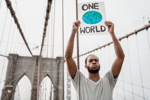 Free A man holds a "One World" sign on the Brooklyn Bridge, symbolizing unity and activism. Stock Photo