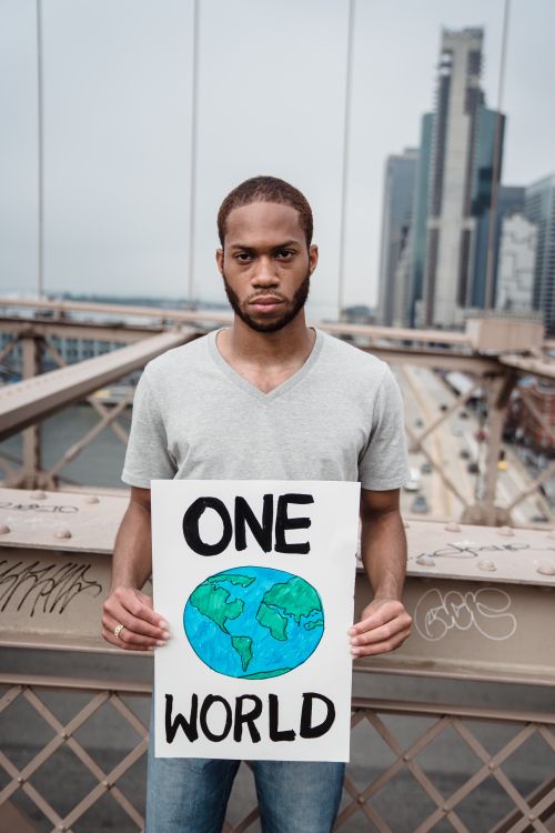 Free A man stands on a bridge holding a 'One World' placard, symbolizing unity and environmental awareness. Stock Photo