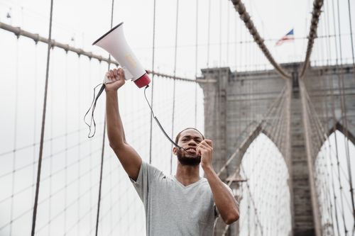 Free Person standing on Brooklyn Bridge holding a megaphone, symbolizing protest. Stock Photo