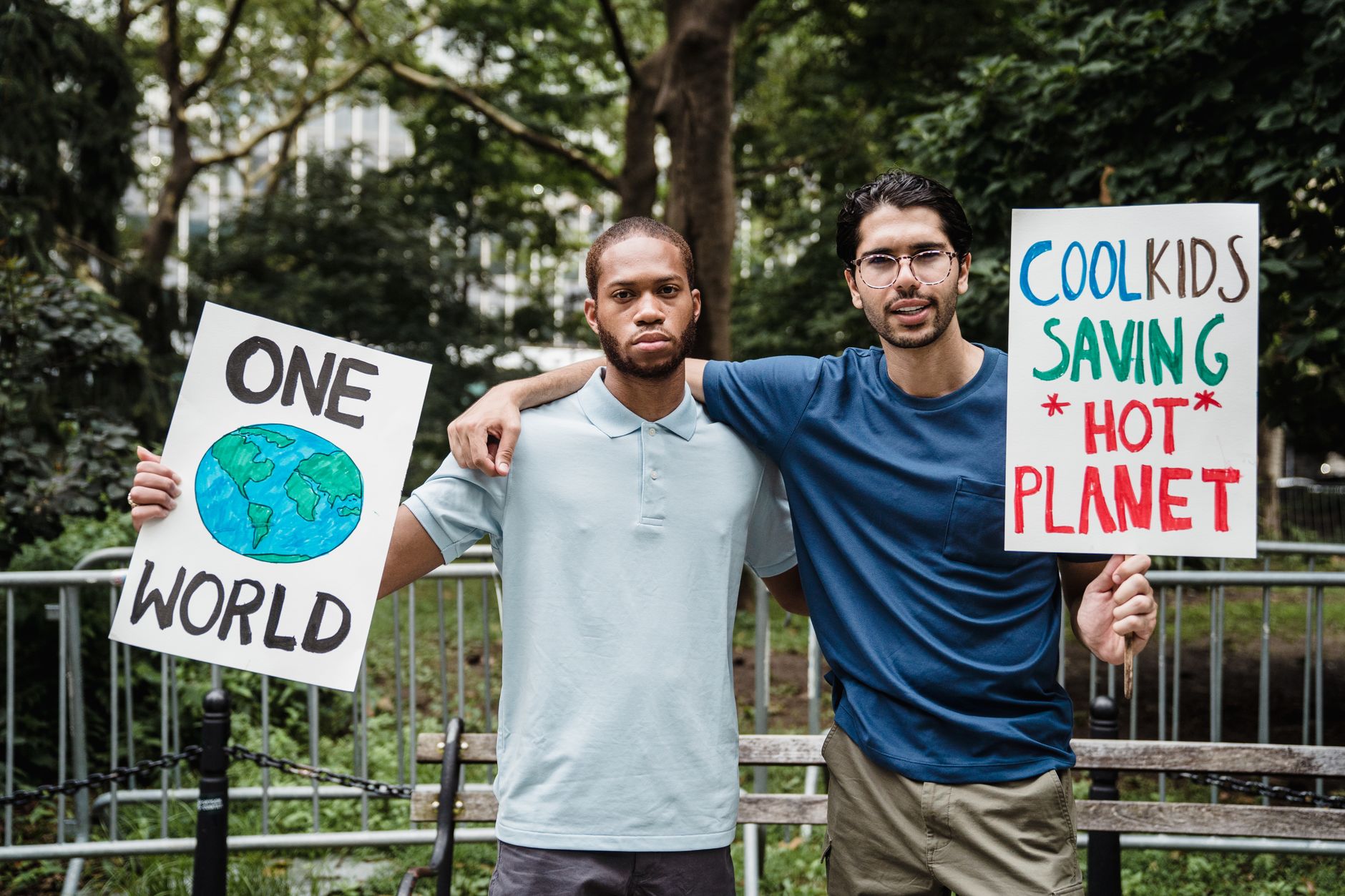 Two men at a protest holding environmental signs promoting climate action in a park setting.