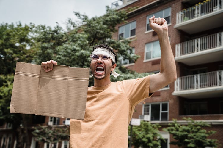 Young Man Standing In Street With Void Cardboard Banner And Calling