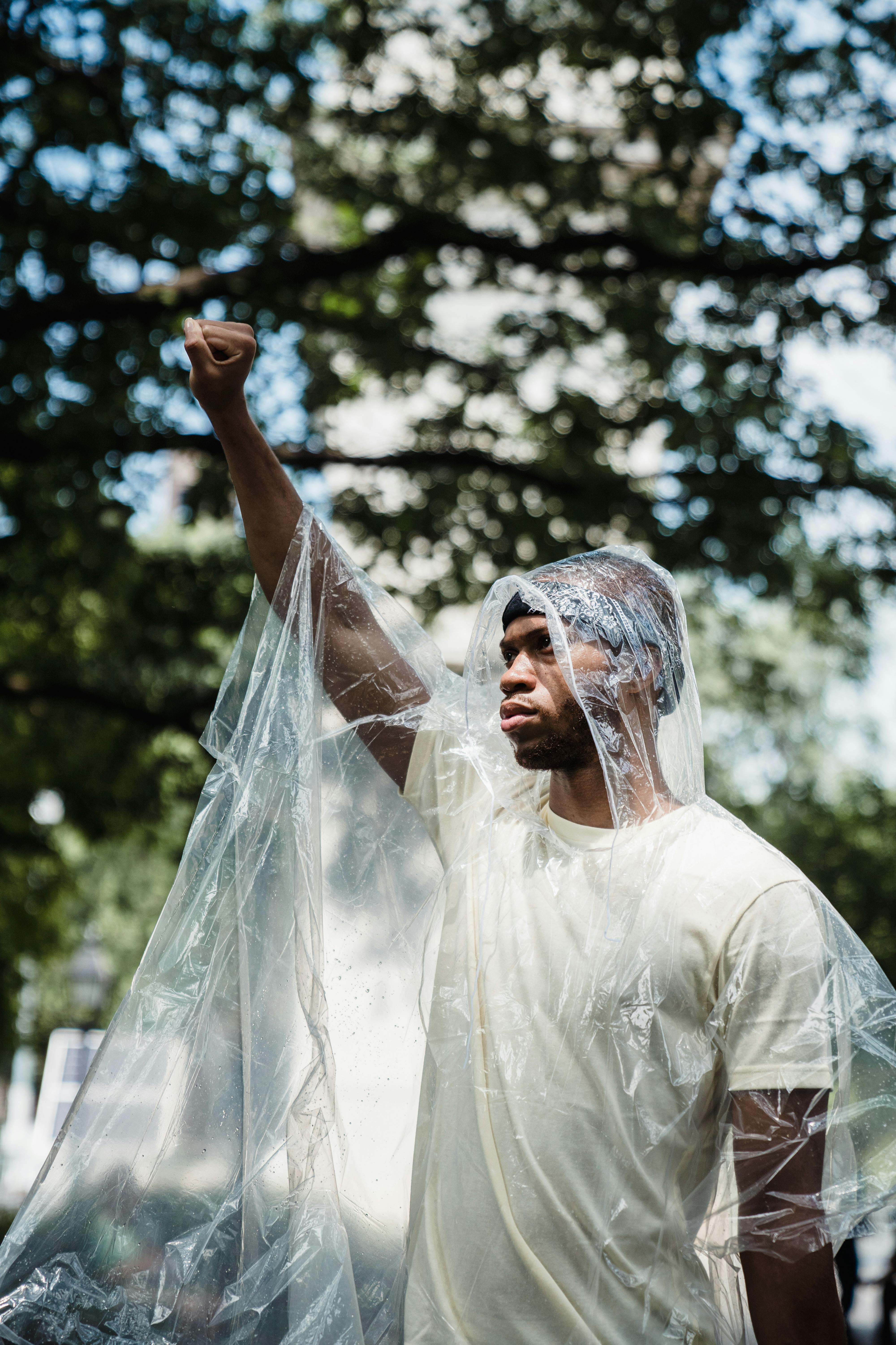 A man protesting plastic pollution with a raised fist covered in plastic outdoors.