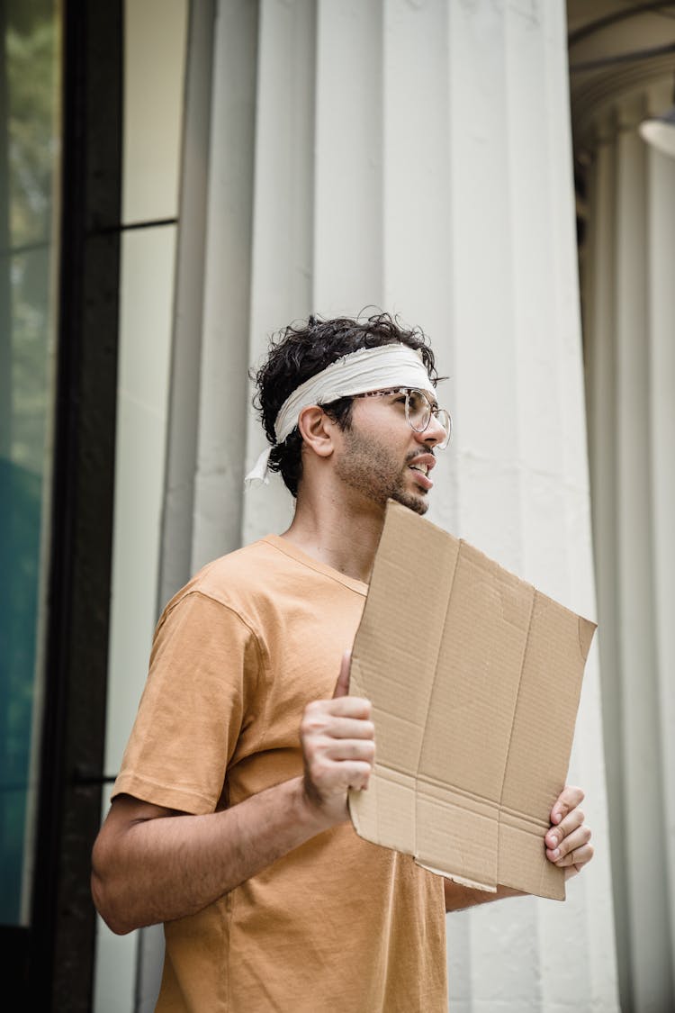 Young Man Standing At Column With Blank Cardboard In Hands