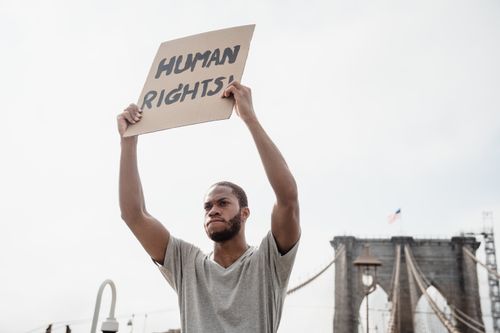 Free An activist raising a sign for human rights in front of the Brooklyn Bridge in daylight. Stock Photo