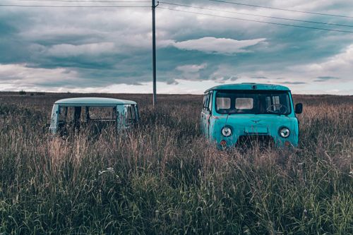 Free Two vintage vans, abandoned in an overgrown field, under a dramatic cloudy sky. Stock Photo