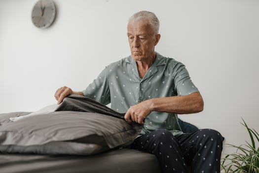 Elderly man carefully making bed, showcasing daily lifestyle routine indoors.