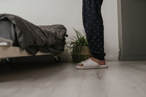 Free Side view of a person standing beside a bed wearing cozy slippers in a modern bedroom. Stock Photo