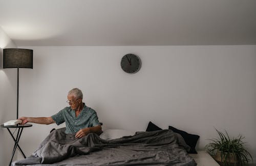 An Elderly Man Getting a Book from a Bedside Table