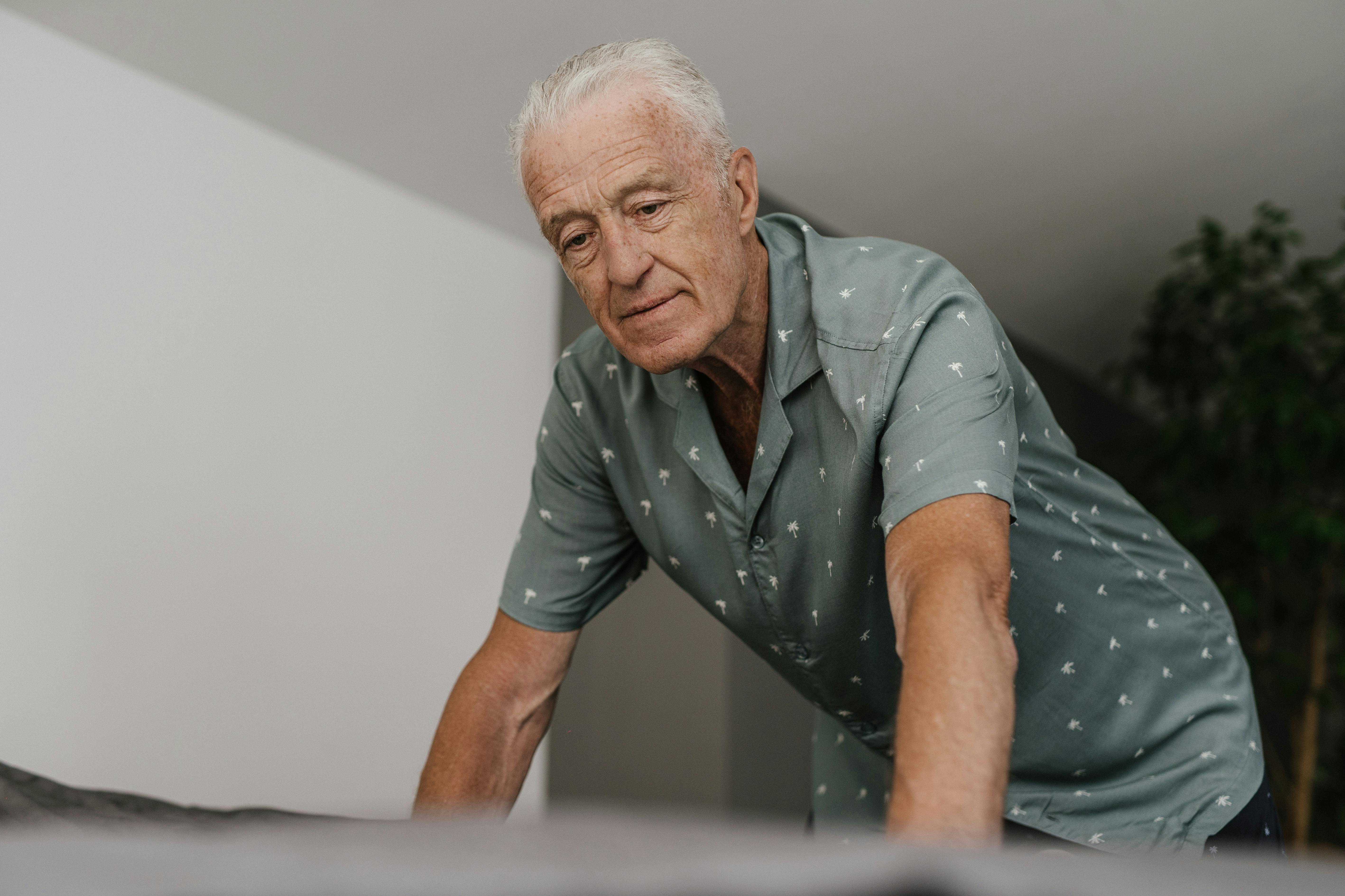 Senior man wearing a casual shirt indoors, showcasing thoughtful expression and engaged posture.