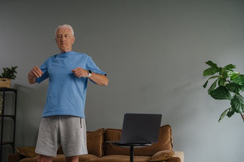 Free Elderly man doing exercise at home in front of a laptop, wearing a smartwatch. Stock Photo