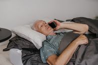 Man Lying on Bed Holding Black Smartphone