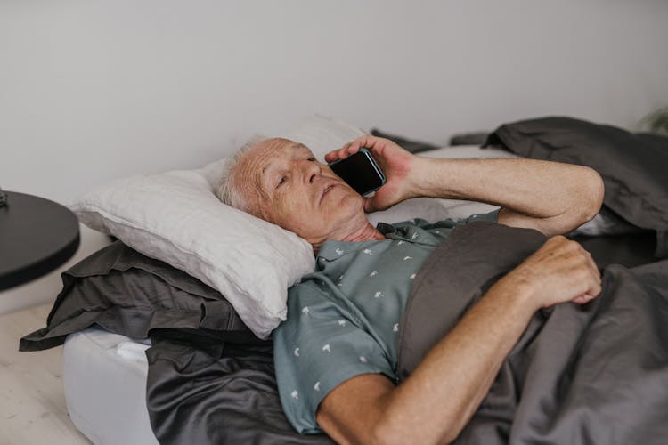 Man Lying On Bed Holding Black Smartphone