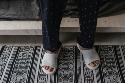 Free A person stands in soft slippers and polka dot pajamas on a patterned rug. Stock Photo