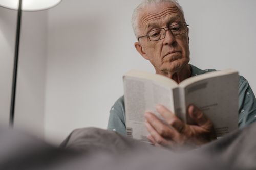 Free Elderly man with glasses reading book indoors, focused expression. Stock Photo