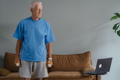 Free Senior man lifting dumbbells at home, staying fit with an online workout session. Stock Photo