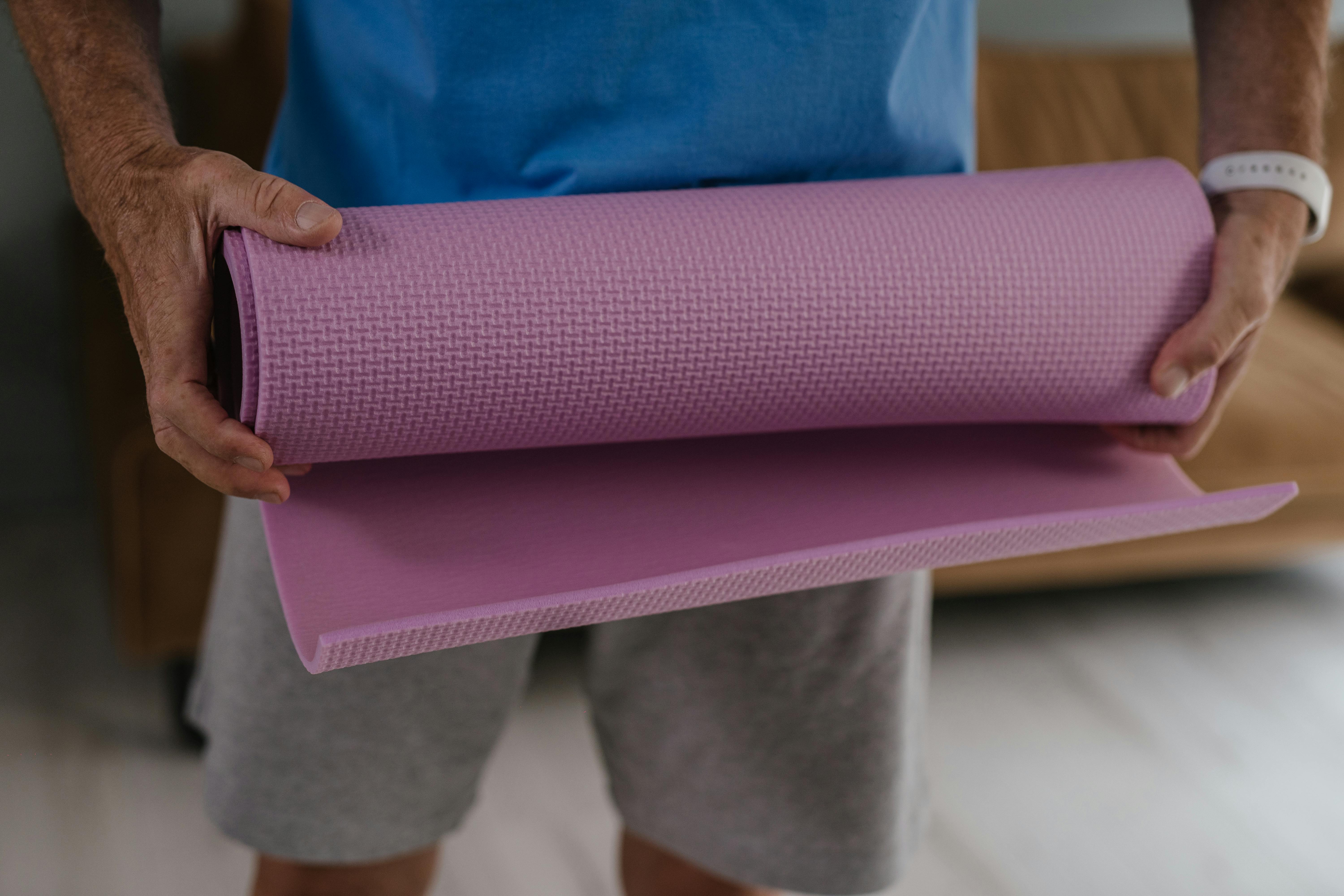 Adult man holding a pink yoga mat, preparing for a fitness routine at home.