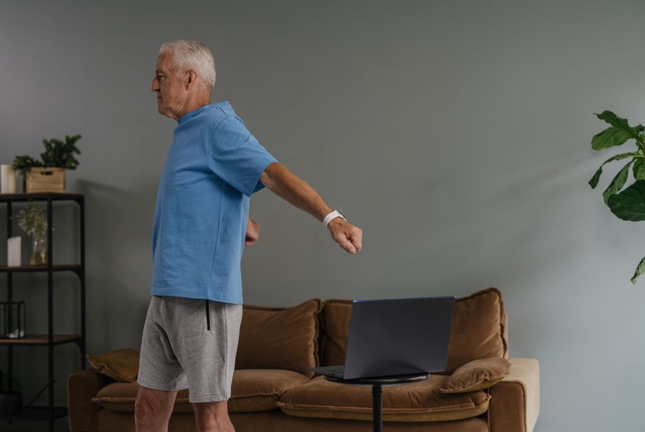How Garmin Body Battery Predicts Your Energy Levels Daily Elderly man stretching indoors while watching laptop, promoting active lifestyle.