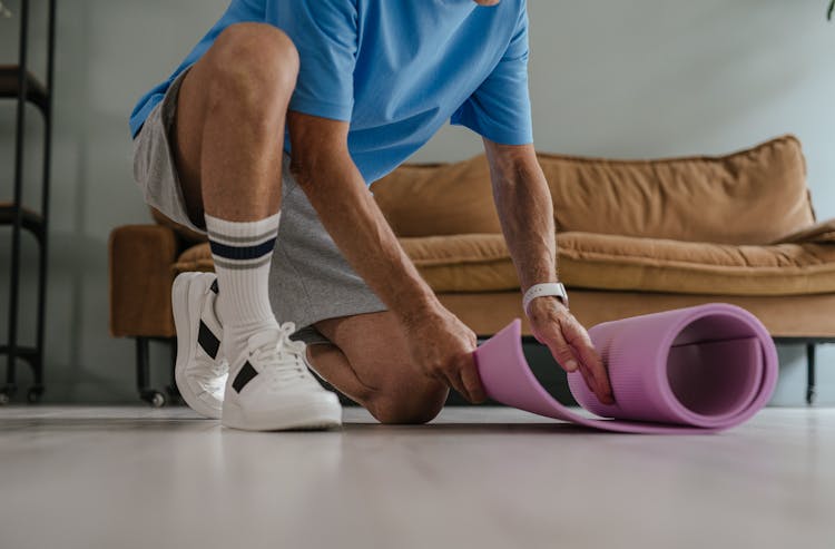 Man In Black And White Shoes And Socks Putting Purple Yoga Mat On Floor 